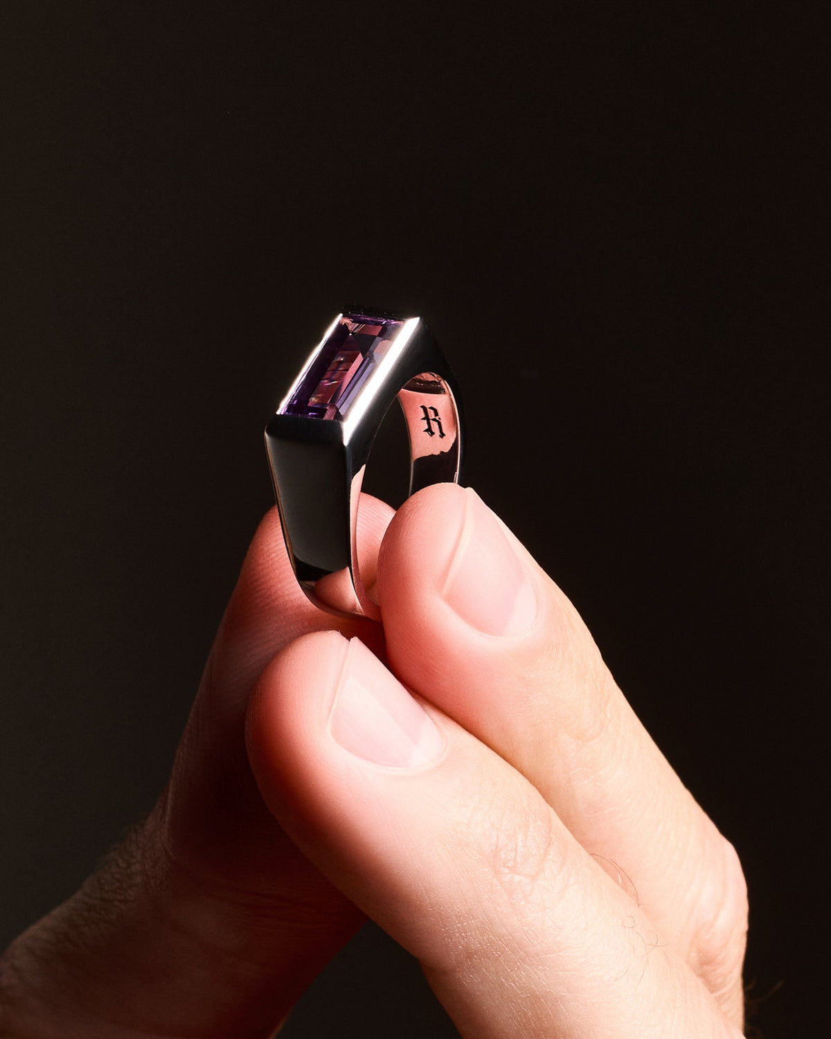 Close-up of a person holding the Amethyst Ring, highlighting the natural baguette-cut amethyst stone set in a high-polish silver rhodium-plated setting.